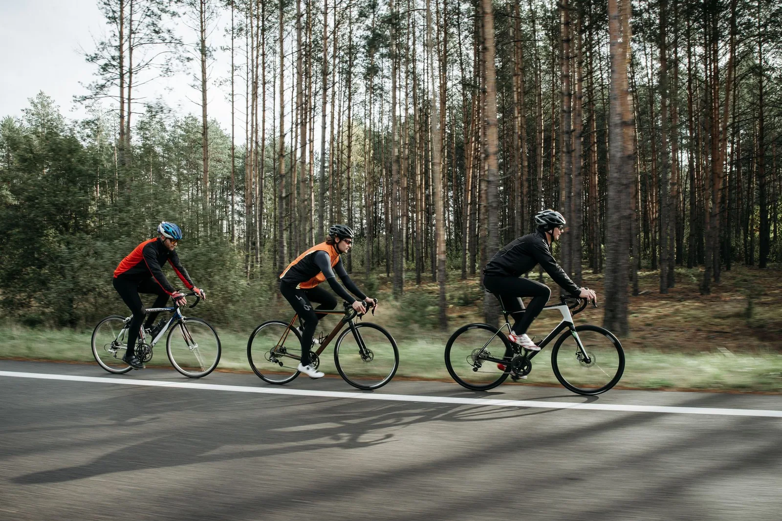 Kolme maantiepyöräilijää ajaa metsän reunustamaa tietä