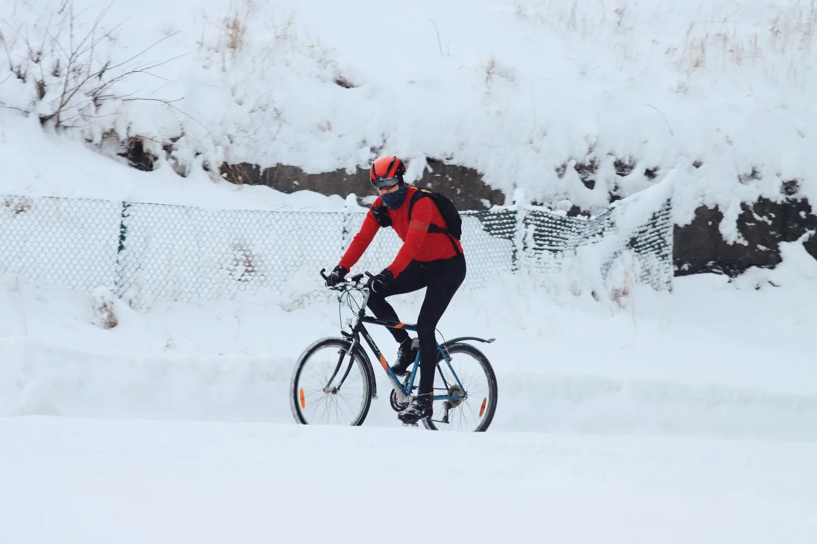 Pyöräilijä ajaa lumisella tiellä punaisessa takissa ja kypärässä