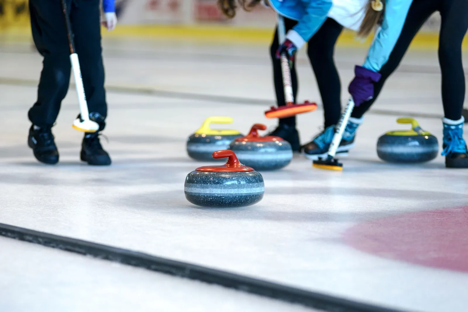 Curling-pelaajat pyyhkivät jäätä harjoilla kivien edessä