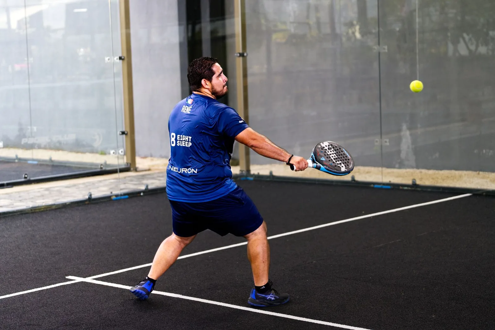 Padel-pelaaja valmistautuu lyöntiin mailalla lasiseinäisellä kentällä