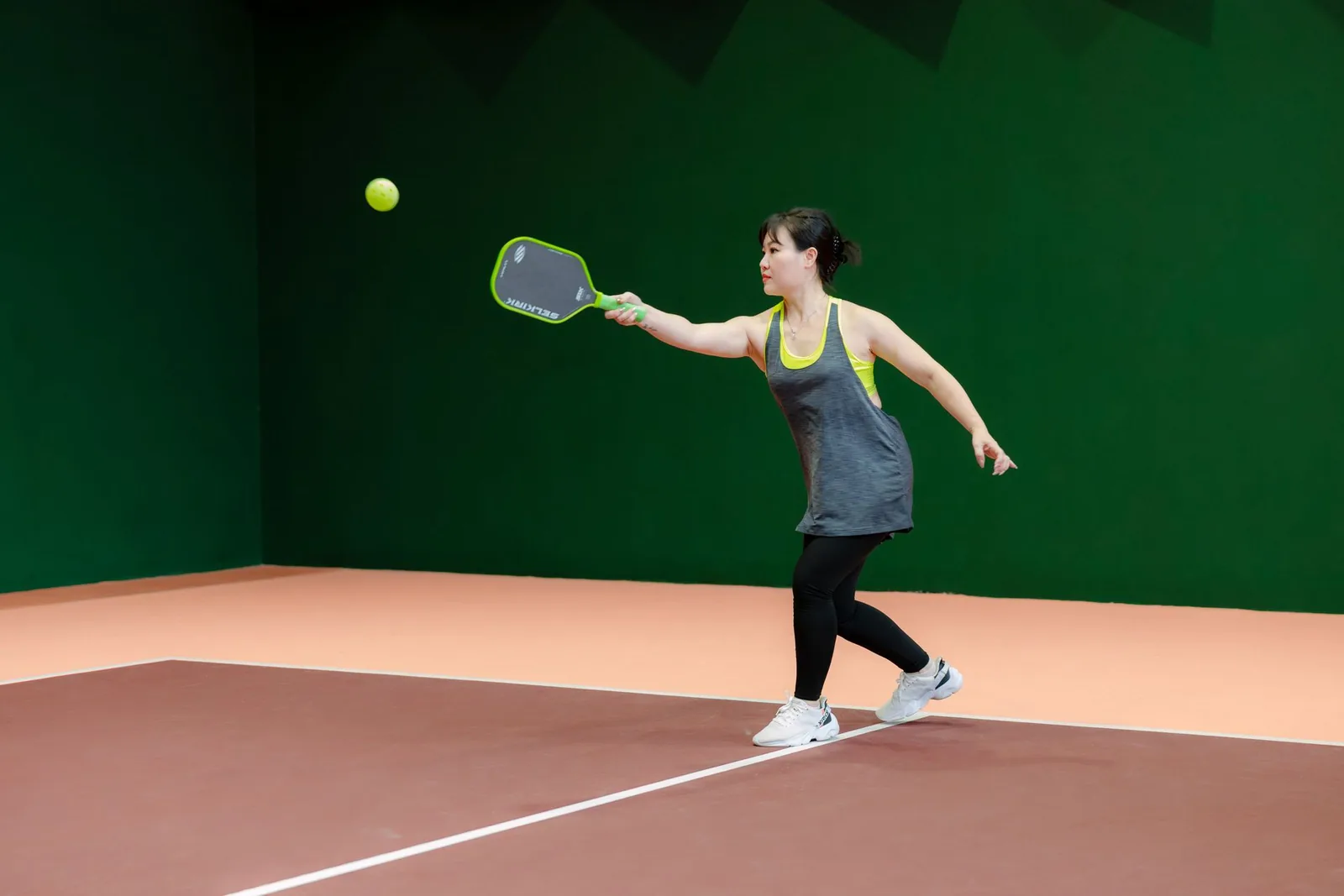 Pelaaja lyö pickleball-pallon mailalla sisäkentällä