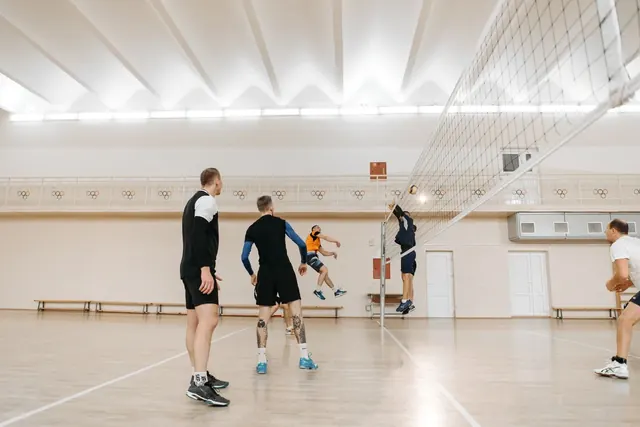 Aikuiset pelaavat lentopalloa liikuntasalissa