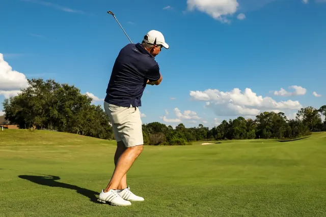 Golfaaja heiluttaa mailaa kentällä sinisen taivaan alla