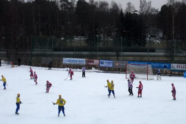Jääpallo-ottelu ulkojäällä, pelaajat keltaisissa ja punaisissa asuissa