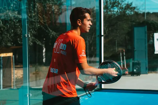 Padel-pelaaja valmistautuu lyöntiin lasiseinän vieressä