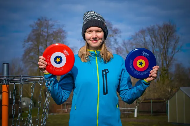 Hymyilevä pelaaja pitää käsissään kahta frisbeegolfkiekkoa