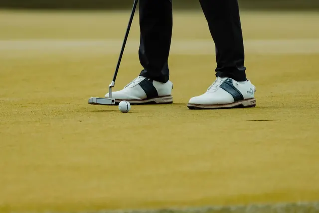 Golfkengät jalassa pelaajalla putterin kanssa viheriöllä