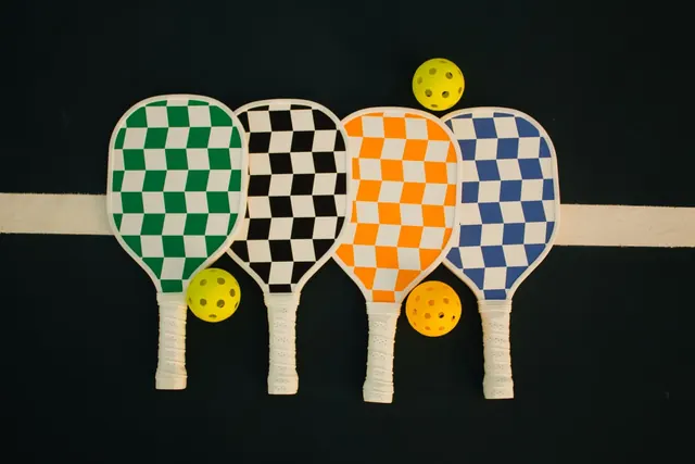 Neljä ruutukuvioista pickleball-mailaa ja keltaisia palloja
