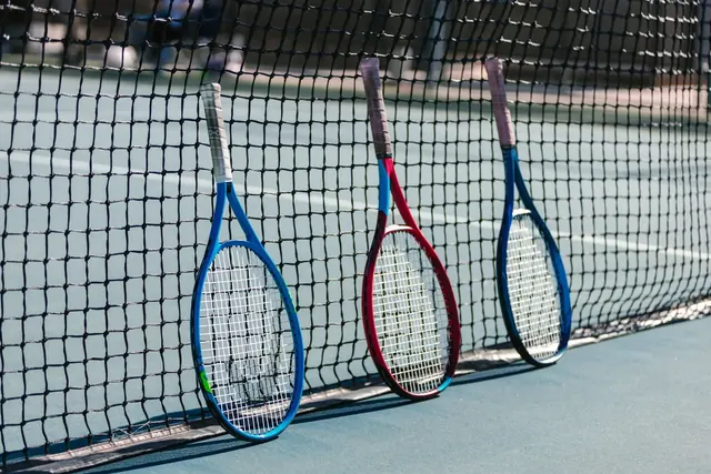 Kolme tennismailaa nojaa tennisverkkoon