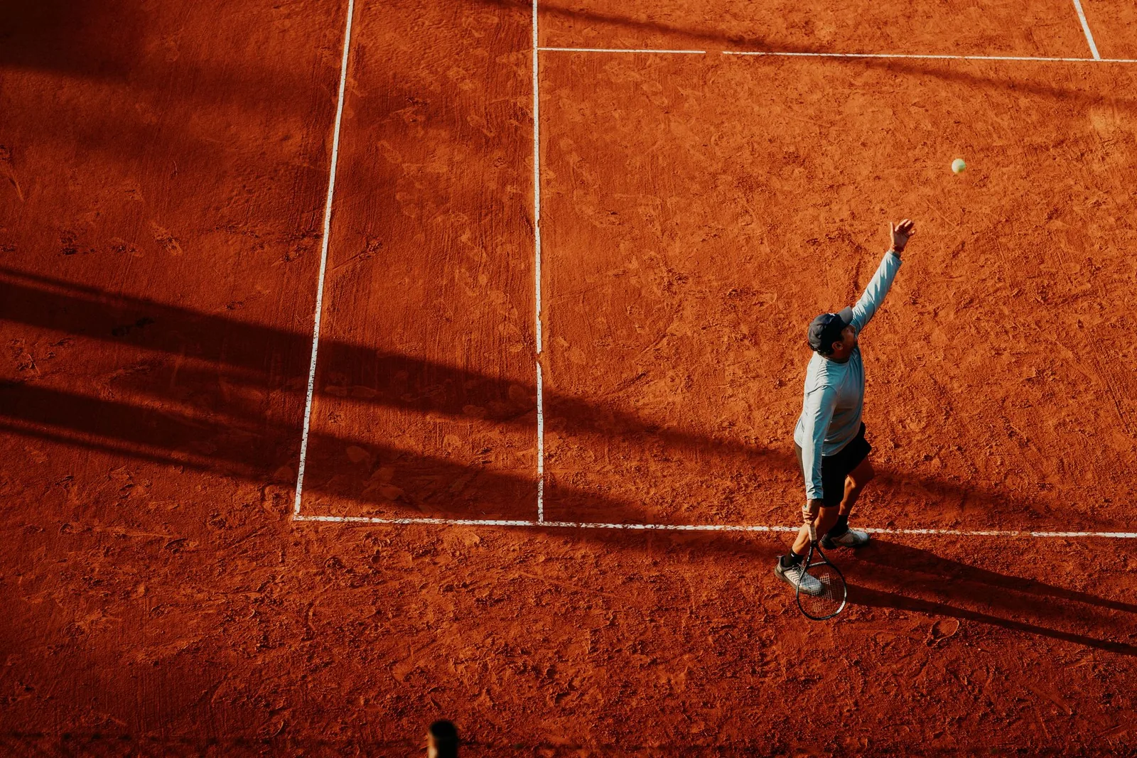 Tennispelaaja tekee syöttöä punasoraisella kentällä