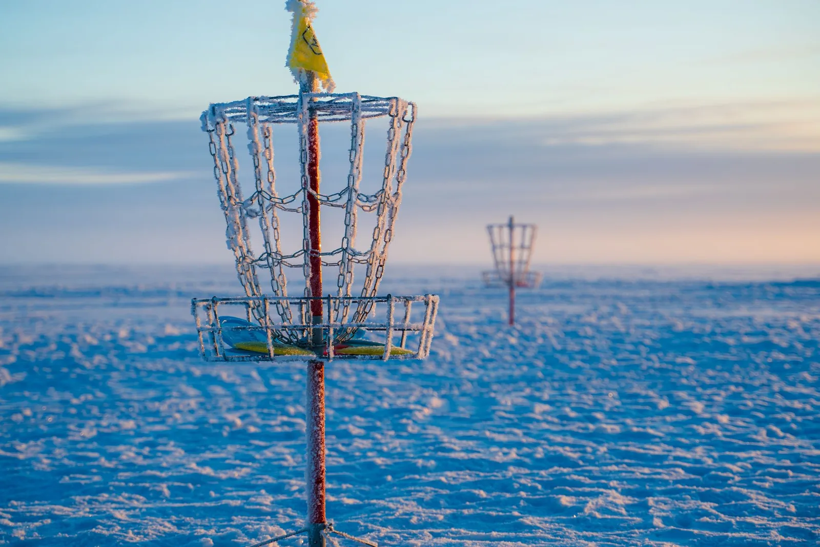 Frisbeegolfkori lumisella kentällä auringonlaskun aikaan